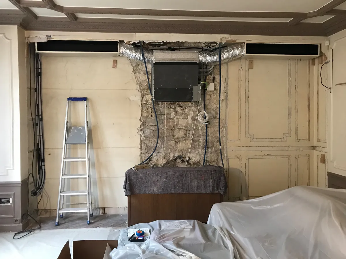 Avant travaux : mur de salon ouvert, gaine de climatisation et câblage apparents, boiseries anciennes déposées