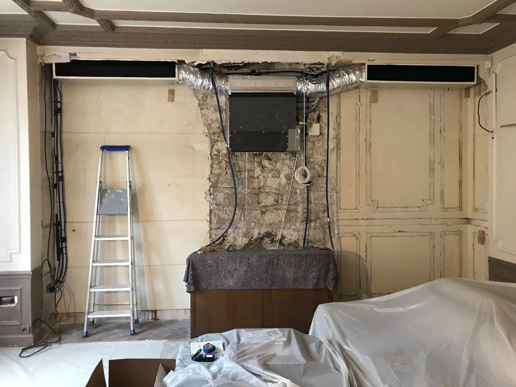 Avant travaux : gaine de climatisation et unité technique apparentes, câbles en attente, boiseries en partie déposées, escabeau et meubles bâchés
