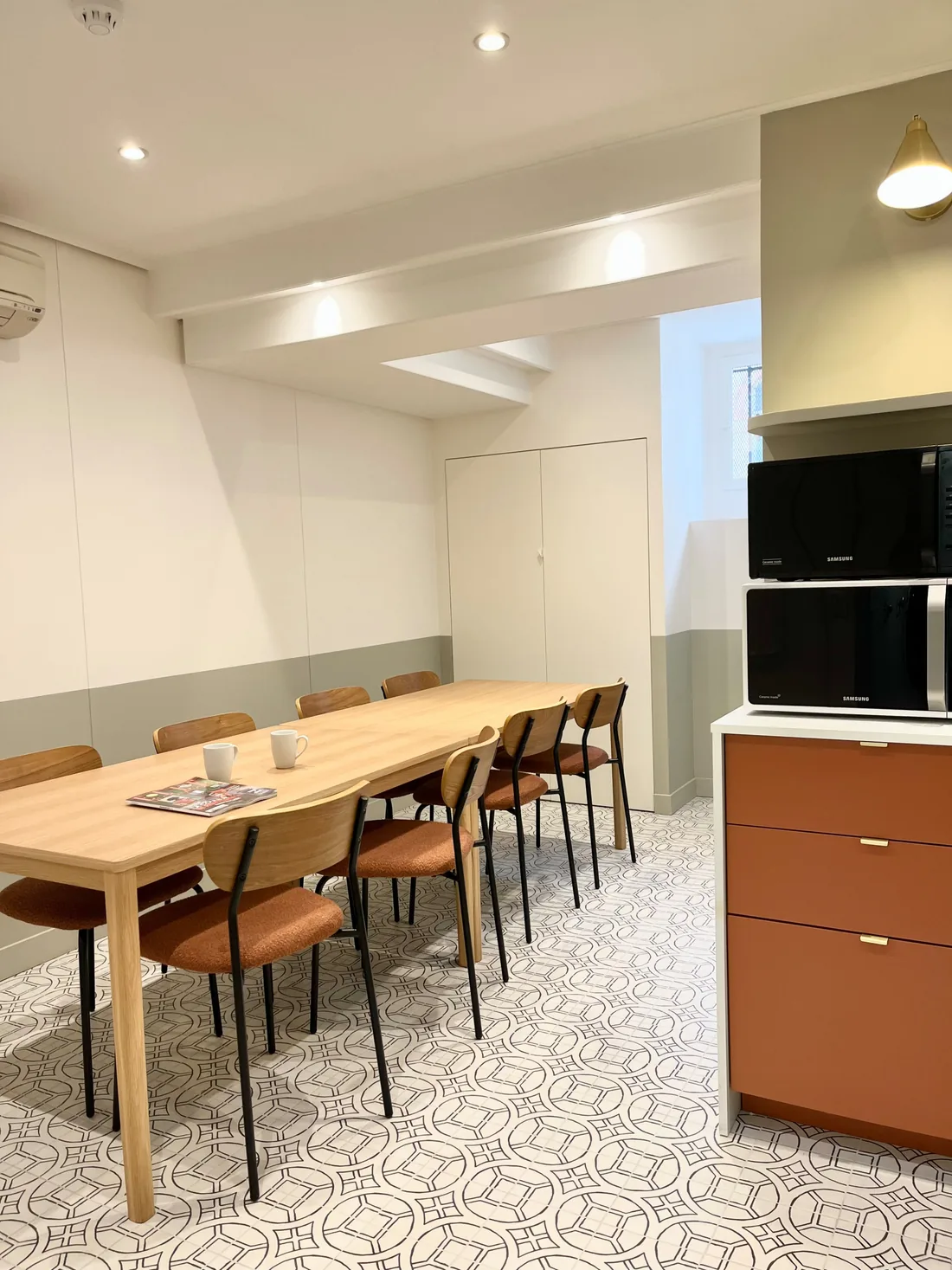 L'espace repas du sous-sol : longue table de bois clair, chaises aux assises cognac, meuble terracotta et sol de carreaux graphiques gris et blancs