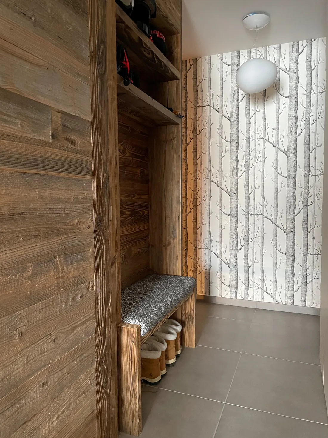 Entrée de l'appartement : banc sur mesure en vieux bois avec rangement à chaussures dessous, étagères hautes pour les casques, et papier peint à motif de troncs de bouleaux