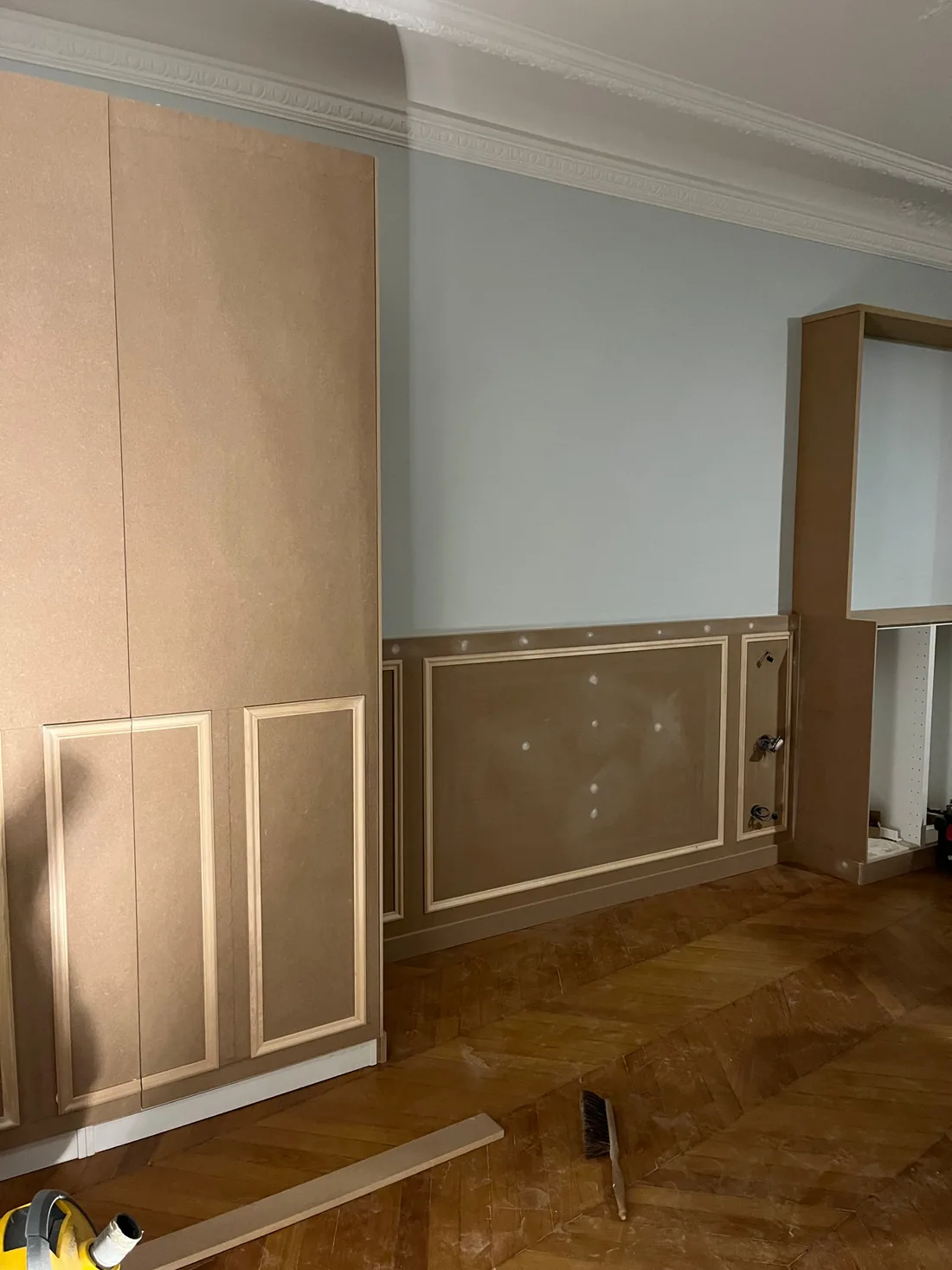Le chantier : caissons et portes des placards en médium brut posés contre les murs, panneaux moulurés avant peinture, parquet point de Hongrie protégé