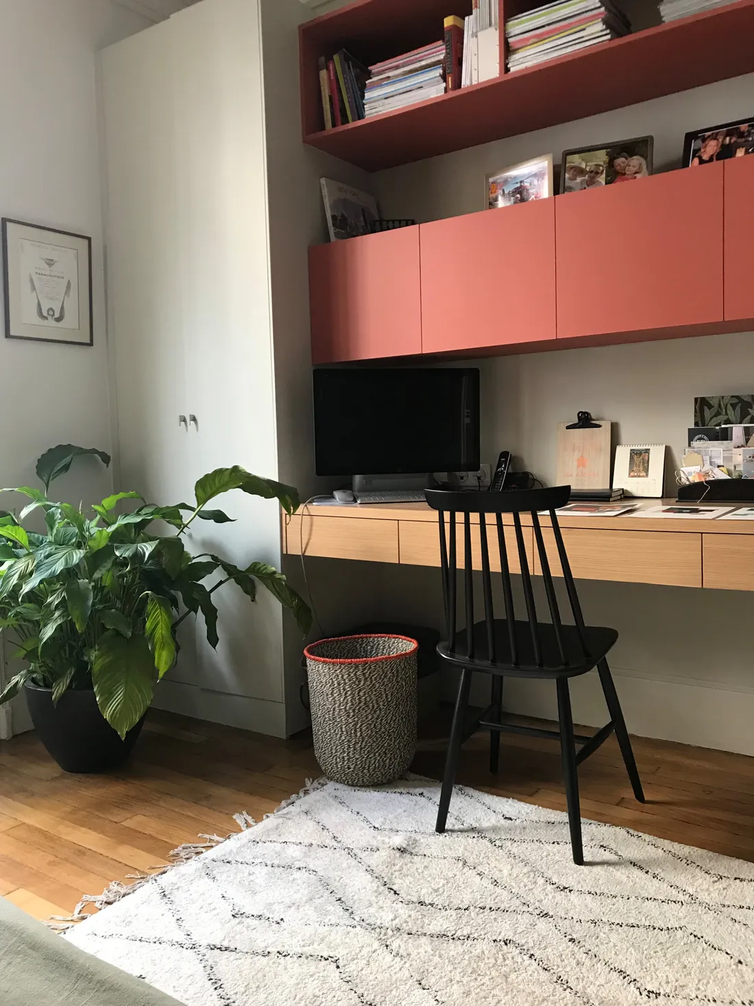 Bureau sur mesure : plan de travail en chêne suspendu à tiroirs, caissons hauts et étagère laqués terracotta, chaise noire à barreaux et tapis berbère