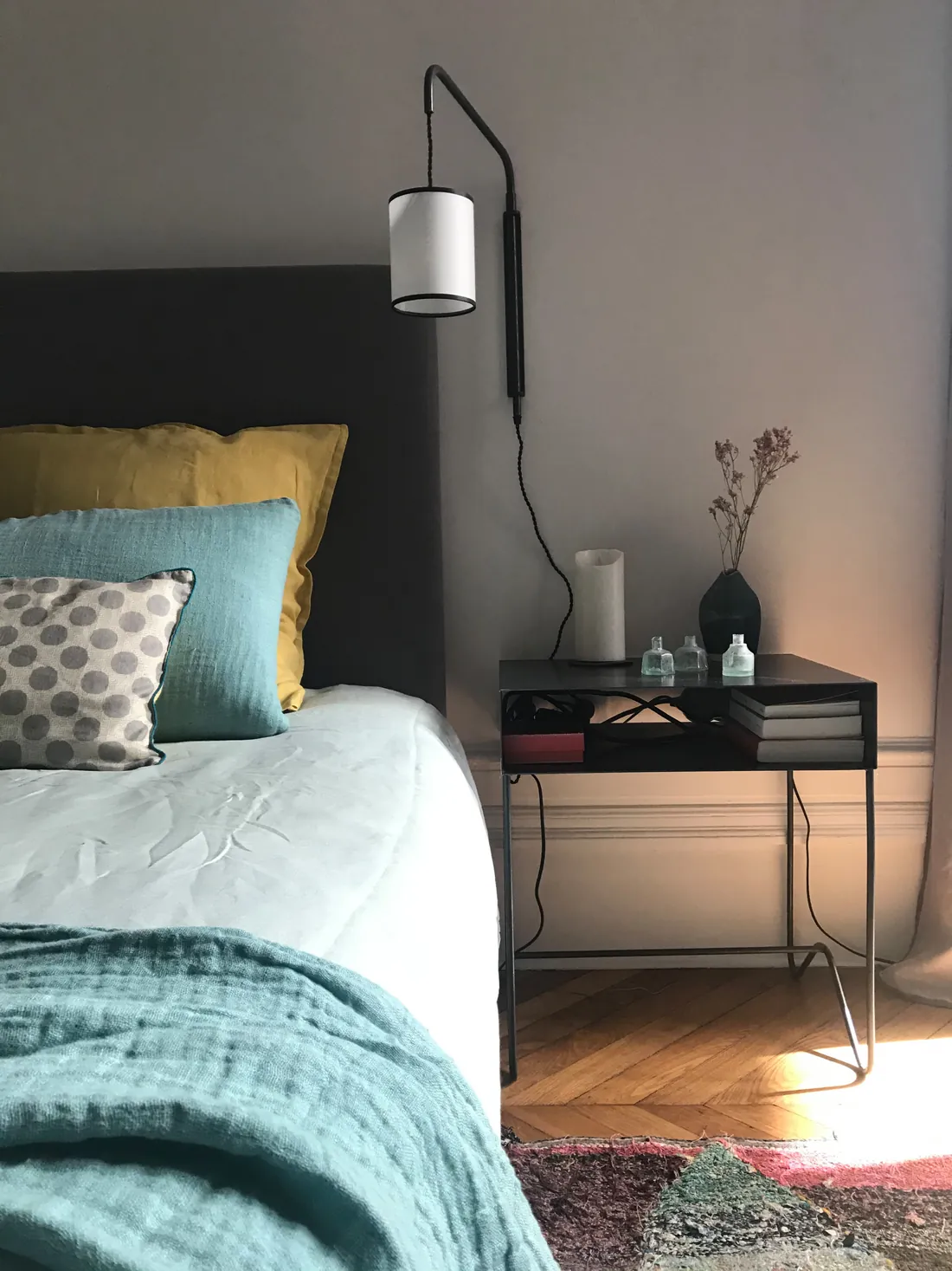 Chambre : tête de lit tapissée gris anthracite, linge de lit bleu canard et jaune moutarde, applique liseuse noire et chevet en métal noir