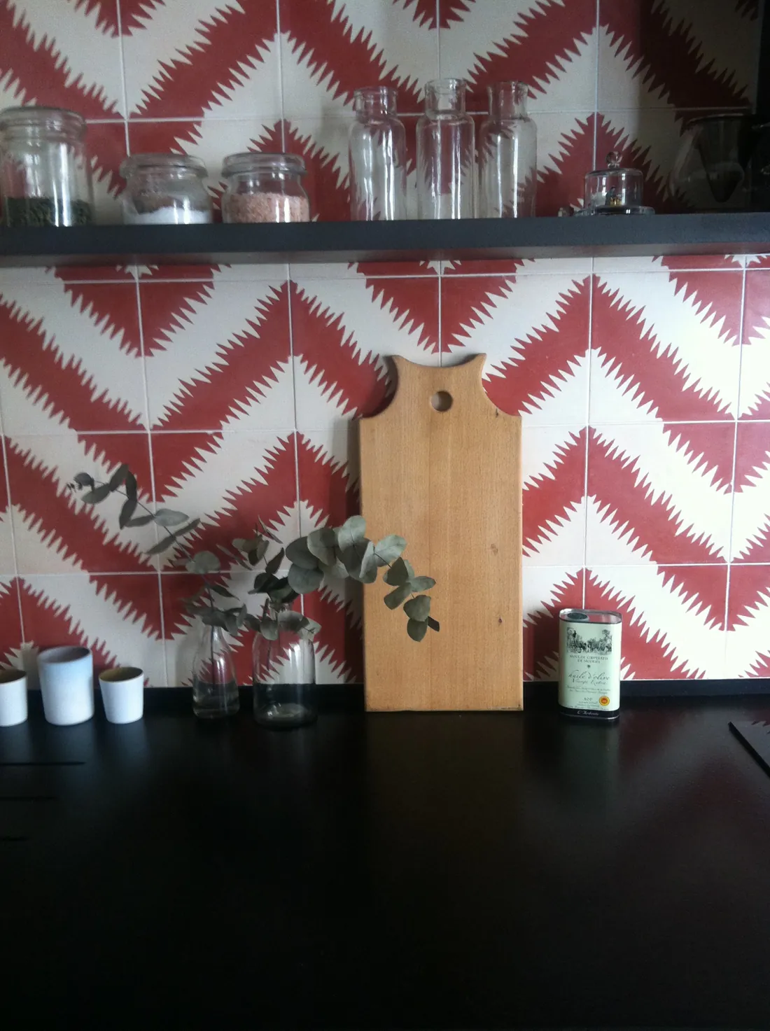 Détail de la crédence de cuisine en carreaux de ciment à chevrons rouges et blancs, plan de travail noir et étagère noire garnie de bocaux en verre