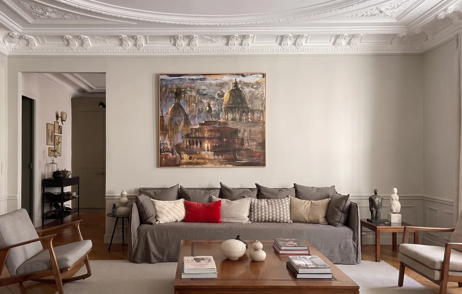 Le salon de l'appartement haussmannien vu en largeur : corniche sculptée de guirlandes et d'instruments, grand tableau de coupoles, canapé gris en housse de lin, plafonnier noir à bras orientables et parquet à point de Hongrie