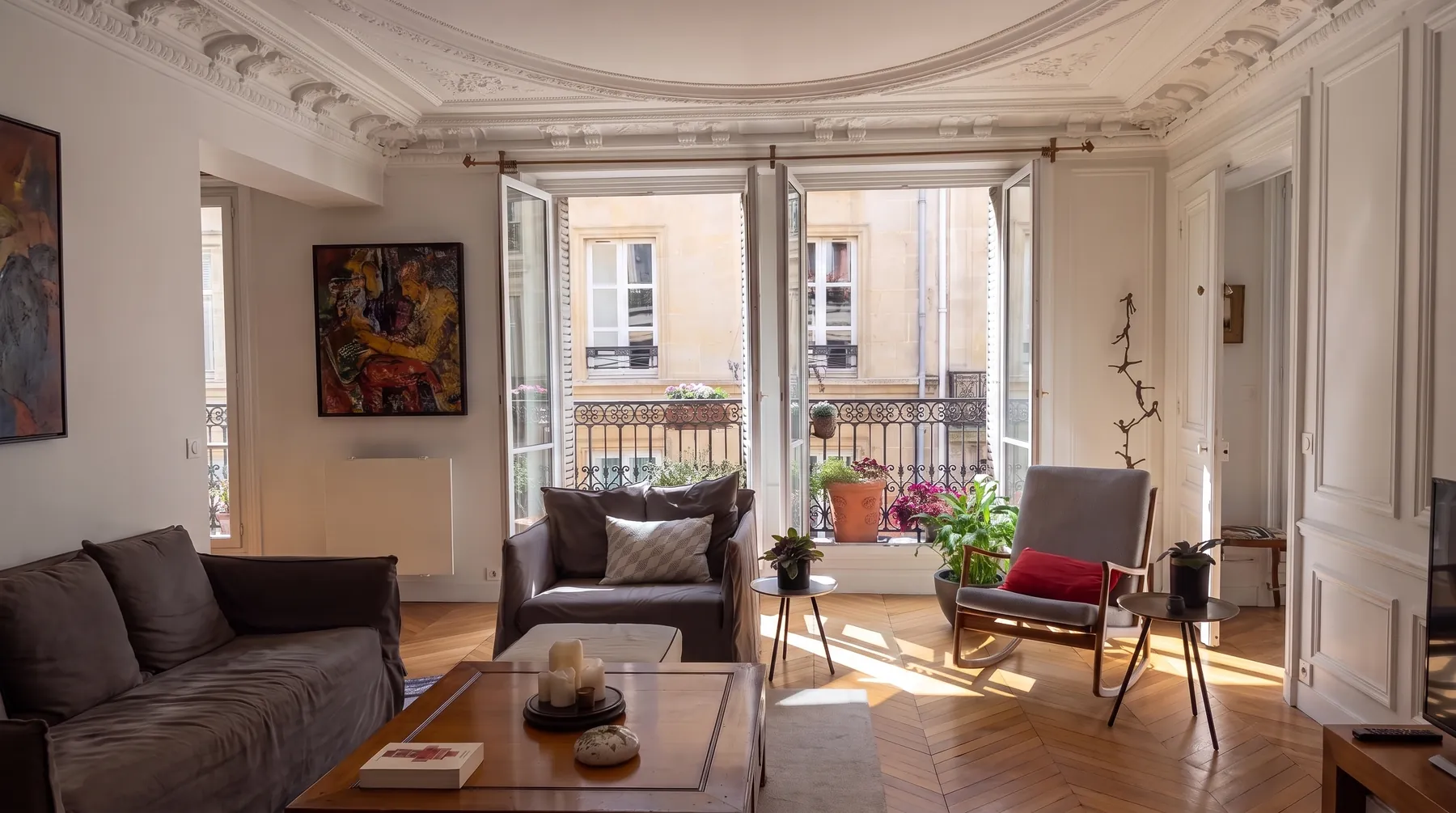 Le salon vu en largeur : corniche moulurée, parquet à point de Hongrie, fenêtres ouvertes sur un balcon en fonte et façade en pierre de taille en vis-à-vis