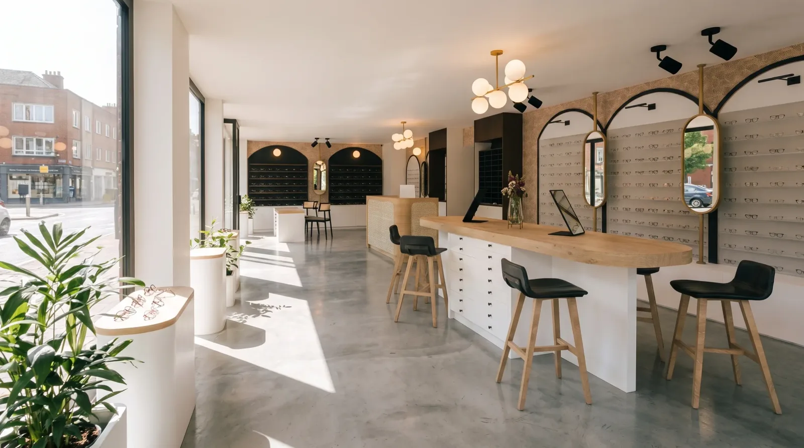 Vue du projet : le magasin d'optique en enfilade, présentoirs muraux à arches noires, table d'essayage centrale en bois clair avec tabourets, suspensions à globes de laiton et vitrine ouvrant sur la rue