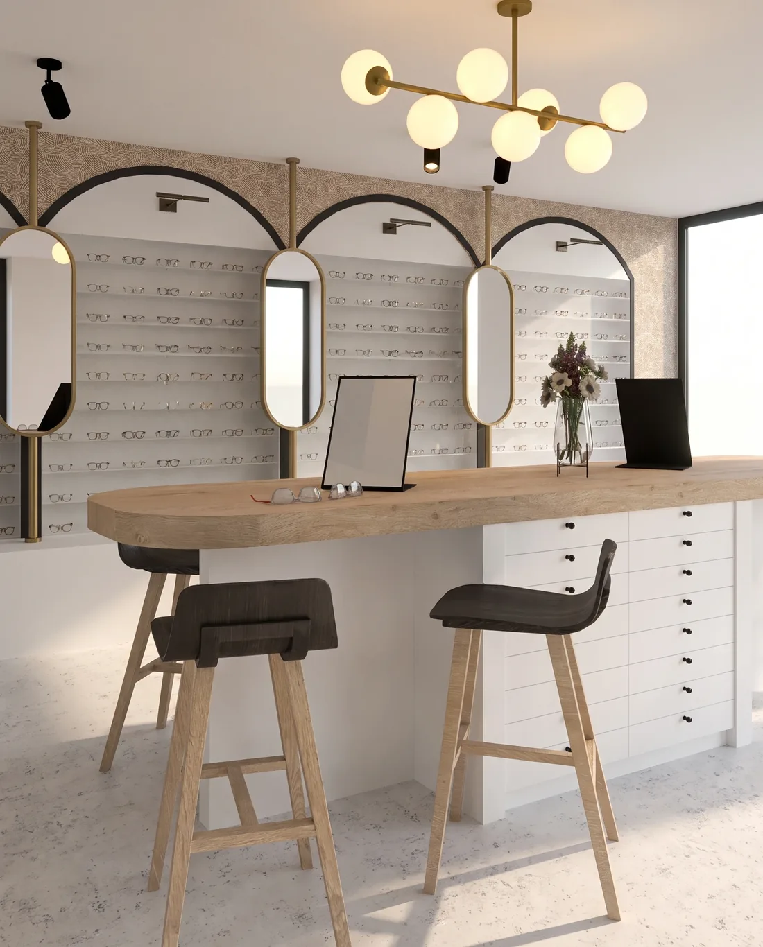Vue du projet : la table d'essayage centrale en bois clair, tabourets à assise noire, miroirs de table, tiroirs blancs à boutons noirs en soubassement et suspension à globes de laiton