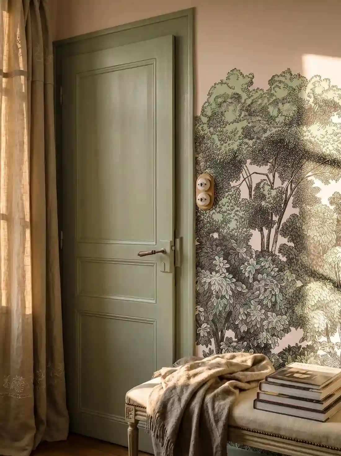 Détail du raccord entre une porte ancienne peinte en vert de gris, avec sa poignée de laiton, et le papier peint panoramique de forêt où l'on distingue deux hiboux perchés dans les branches