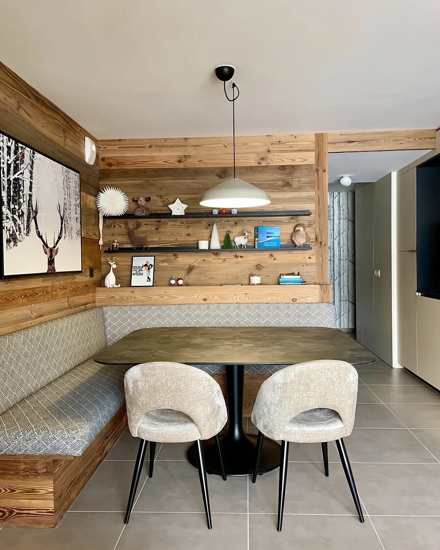 Coin repas d'un appartement de chalet aux Gets : banquette et mur en bois de récupération, table ovale et chaises en laine bouclée