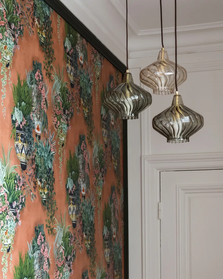Panneau de papier peint panoramique orange à motifs de vases fleuris, encadré de noir, et trois suspensions en verre fumé dans des bureaux haussmanniens