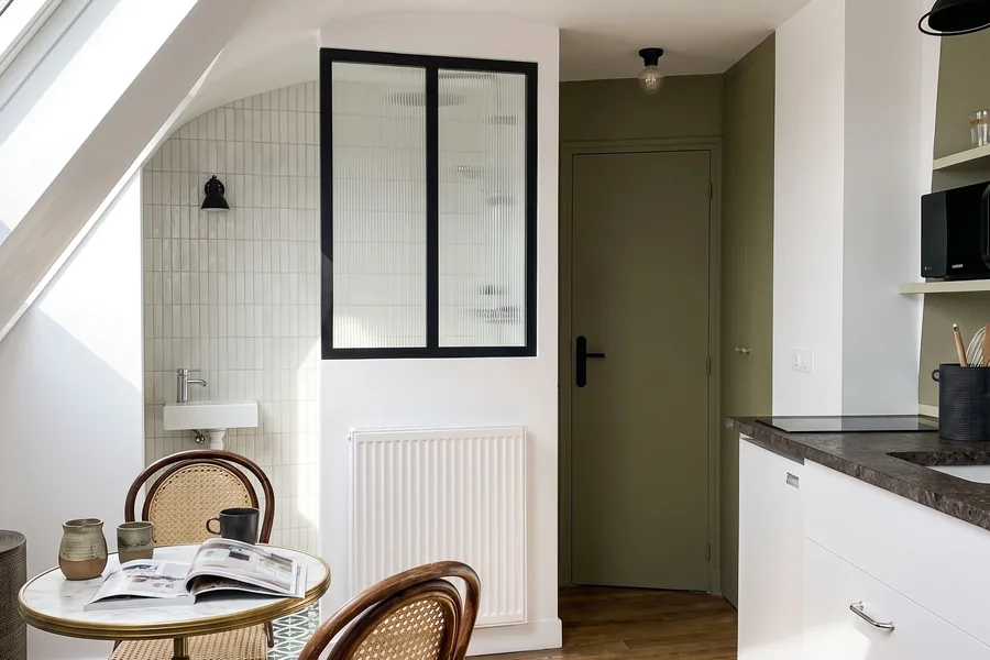 Studio de 10 m² sous les toits de Paris : verrière, coin repas avec chaises en rotin et cuisine intégrée sous la pente