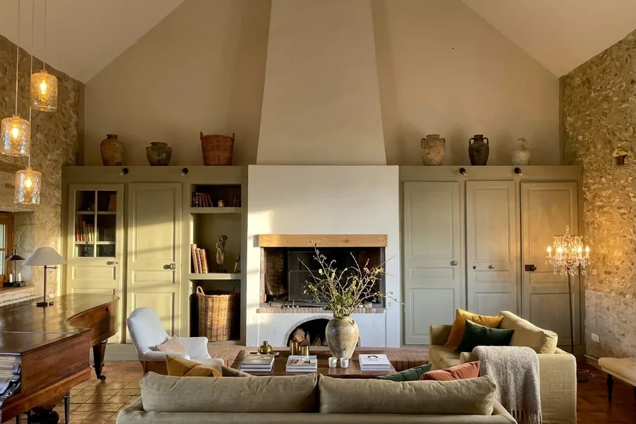 Séjour sous charpente d'une maison de campagne rénovée : cheminée blanche, murs en pierre, grands canapés en lin