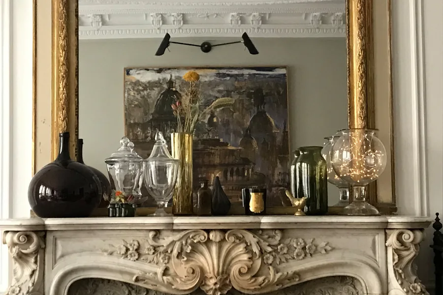 Cheminée en marbre sculpté d'un appartement haussmannien parisien, verrerie ancienne et tableau posé sur le trumeau