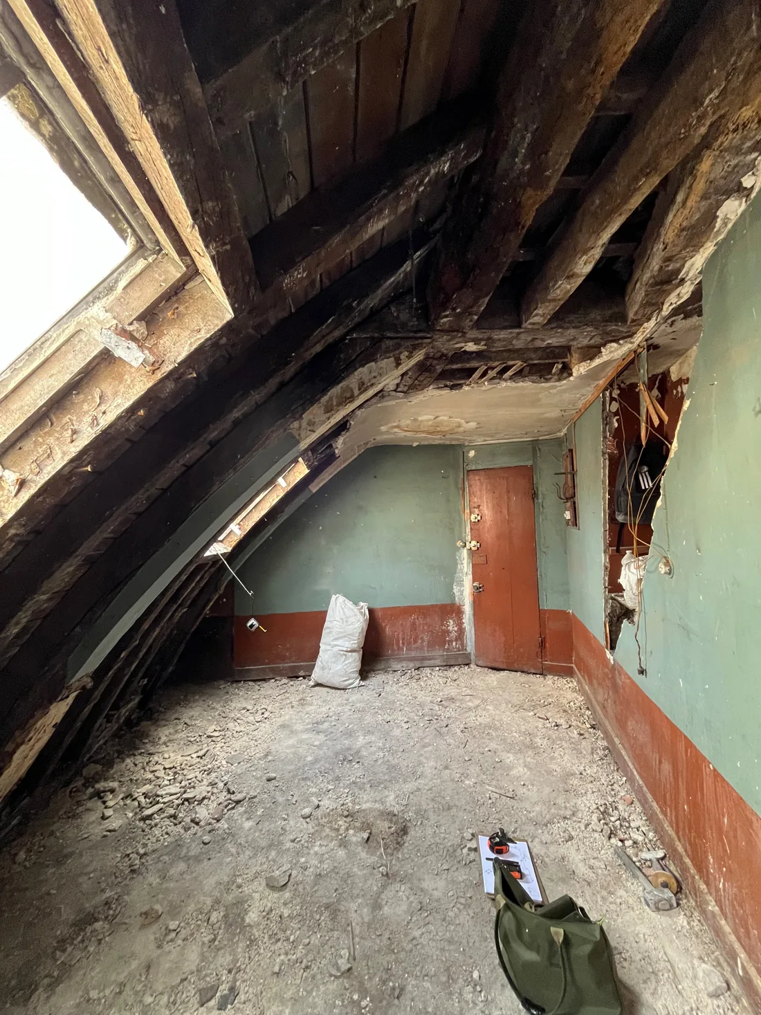 Avant travaux : la charpente ancienne apparente au-dessus de la fenêtre de toit, bois sombres, plancher brut et porte rouge au fond