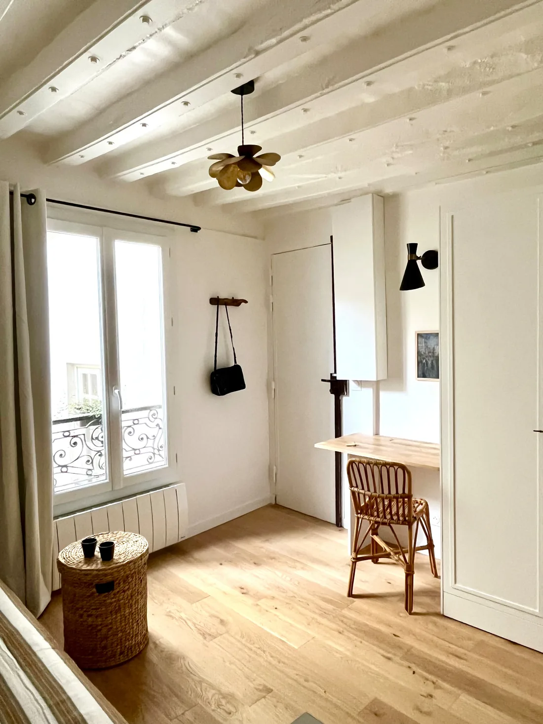 Le coin bureau : tablette murale rabattable près de la fenêtre, chaise de rotin, applique noire orientable et sac suspendu à une patère