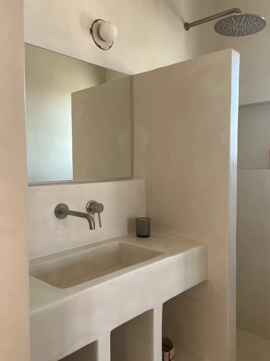 Salle d'eau en enduit clair : vasque maçonnée d'un seul tenant, paroi de douche pleine, robinetterie discrète et miroir posé sur la maçonnerie